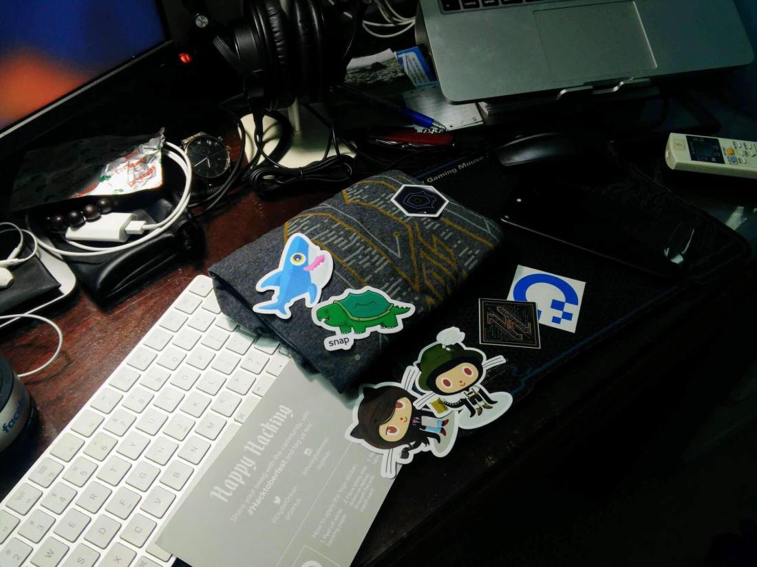 Sticker Octocat, áo thun và quà tặng Hacktoberfest nhận được từ sự kiện công nghệ, bày trên bàn làm việc